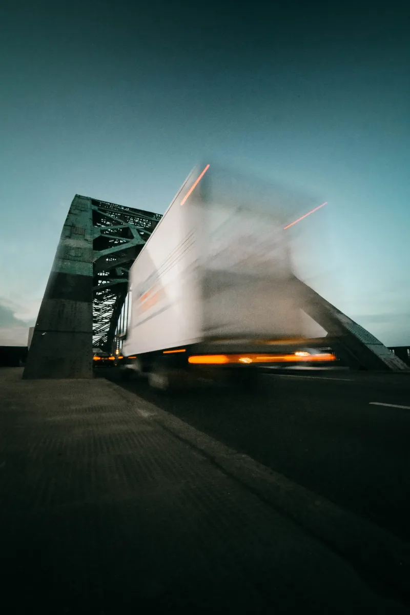 Een vrachtwagen die bij schemer over een stalen brug rijdt.